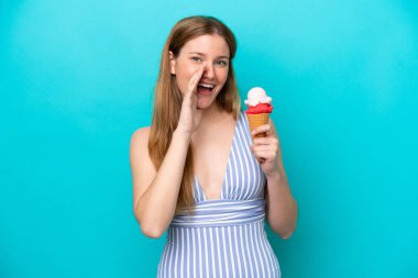 Mavi arka planda izole edilmiş, ağzı açık bir şekilde bağıran mayo giyen beyaz bir kadın dondurma yiyor.