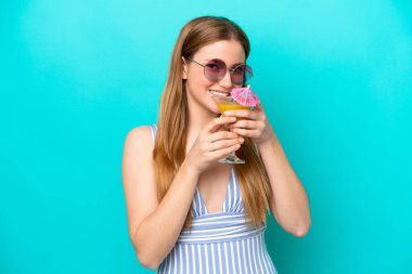 Mavi arka planda mayo giymiş ve elinde kokteyl tutan genç bir kadın.