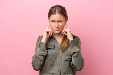 Pembe arka planda izole edilmiş genç beyaz kadın hayal kırıklığına uğramış ve kulaklarını kapatmış.