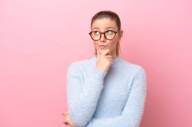 Pembe arka planda izole edilmiş genç beyaz kadın yukarı bakarken bir fikir düşünüyor.