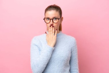 Pembe arka planda izole edilmiş, ağzı elle kaplanmış beyaz bir kadın.