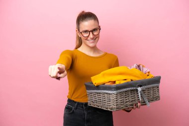 Pembe arka planda izole edilmiş çamaşır sepetini tutan beyaz bir kadın mutlu bir ifadeyle ön tarafı işaret ediyor.