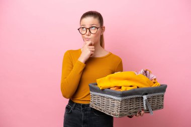 Pembe arka planda izole edilmiş çamaşır sepetini tutan beyaz bir kadın şüpheleri var.