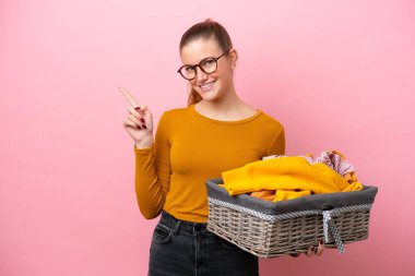 Pembe arka planda izole edilmiş çamaşır sepetini tutan beyaz bir kadın var.