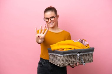 Pembe arka planda izole edilmiş çamaşır sepetini tutan beyaz bir kadın mutlu ve parmakları olan dört kişi sayıyor.