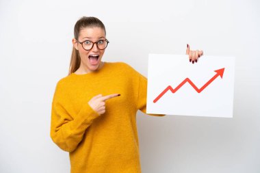 Beyaz arka planda izole edilmiş genç beyaz bir kadın elinde büyüyen bir istatistik okuyla şaşırmış ifade ile bir işaret tutuyor.