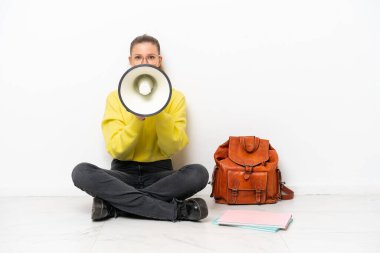 Beyaz arka planda tek başına oturan beyaz tenli genç bir kadın megafonla bağırıyor.