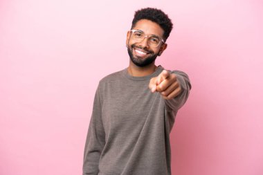 Pembe arka planda izole edilmiş genç Brezilyalı adam mutlu bir ifadeyle ön tarafı işaret ediyor.
