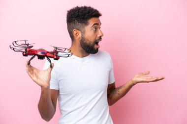 Genç Brezilyalı bir adam pembe arka planda yüzü şaşırmış bir dron tutuyor.
