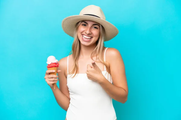 若いですCaucasian女性で水着でコーネットアイスクリーム隔離上の青の背景に親指アップで何か良いことが起こっているので — ストック写真