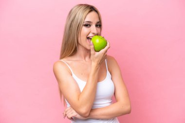 Pretty blonde woman isolated on pink background eating an apple