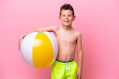 Little caucasian boy holding a beach ball isolated on pink background smiling a lot