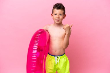 Küçük beyaz bir çocuk pembe arka planda izole edilmiş şişirilebilir bir çörek tutuyor.