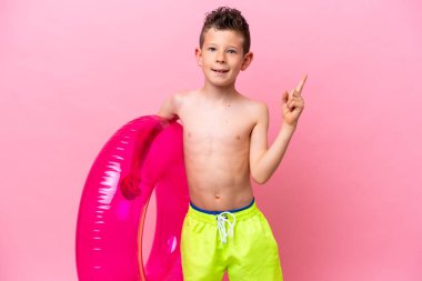 Little caucasian boy holding a inflatable donut isolated on pink background showing and lifting a finger in sign of the best