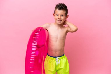 Küçük beyaz çocuk pembe arka planda izole edilmiş şişme bir çörek tutuyor.