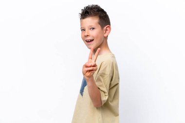 Beyaz arka planda izole edilmiş küçük beyaz çocuk gülümsüyor ve zafer işareti gösteriyor.