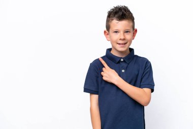 Beyaz arka planda izole edilmiş küçük beyaz çocuk bir ürünü sunmak için kenarı işaret ediyor.