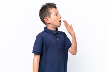 Beyaz arka planda izole edilmiş küçük beyaz çocuk esniyor ve ağzını eliyle kapatıyor.