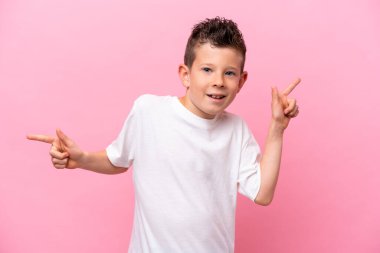 Little caucasian boy isolated on pink background pointing finger to the laterals and happy