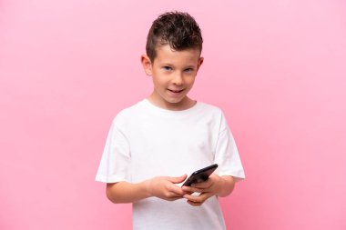 Little caucasian boy isolated on pink background sending a message with the mobile