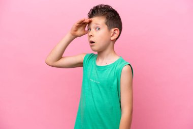 Little caucasian boy isolated on pink background doing surprise gesture while looking front