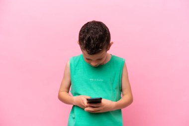 Little caucasian boy isolated on pink background sending a message with the mobile