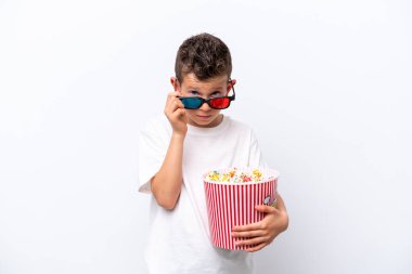 Little caucasian boy isolated on white background surprised with 3d glasses and holding a big bucket of popcorns