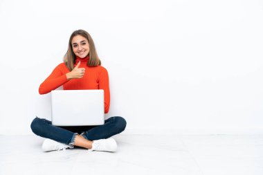 Young caucasian woman sitting on the floor with a laptop giving a thumbs up gesture