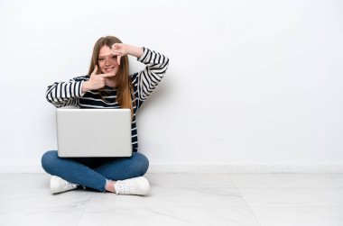 Young caucasian woman with a laptop sitting on the floor isolated on white background focusing face. Framing symbol