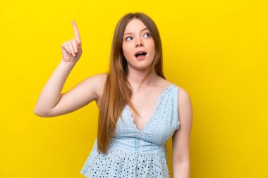 Sarı arka planda izole edilmiş genç beyaz kadın parmağını kaldırarak çözümü bulmaya çalışıyor.