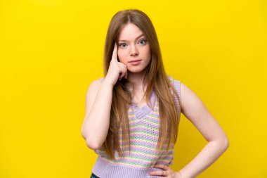 Kafkasyalı genç bir kadın sarı arka planda izole edilmiş bir fikir düşünüyor.