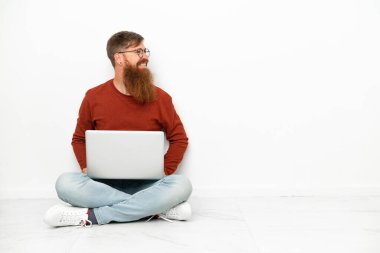 Young reddish caucasian man with laptop isolated on white background looking side