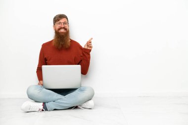 Young reddish caucasian man with laptop isolated on white background pointing finger to the side