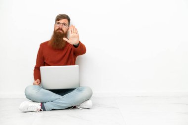 Young reddish caucasian man with laptop isolated on white background making stop gesture