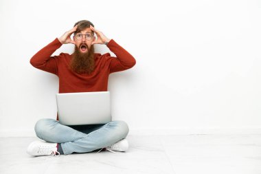 Young reddish caucasian man with laptop isolated on white background with surprise expression