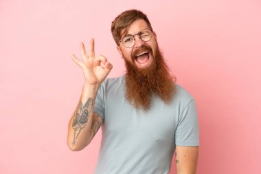 Pembe arka planda izole edilmiş genç, beyaz bir adam parmaklarıyla tamam işareti gösteriyor.