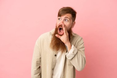 Young reddish caucasian man isolated on pink background shouting with mouth wide open to the side