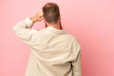 Young reddish caucasian man isolated on pink background in back position and thinking