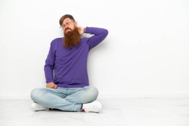 Beyaz arka planda boynu ağrıyan beyaz tenli, beyaz bir adam yerde oturuyor.