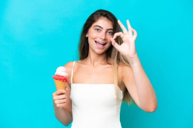 Mavi arka planda izole edilmiş bir dondurma tutan mayo giymiş genç bir kadın parmaklarıyla işaret veriyor.
