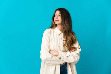 Mavi arka planda izole edilmiş genç beyaz kadın yan tarafa bakıyor.
