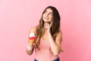 Kornet dondurmalı genç beyaz kadın pembe arka planda izole edilmiş bir şekilde yukarı bakarken bir fikir düşünüyor.