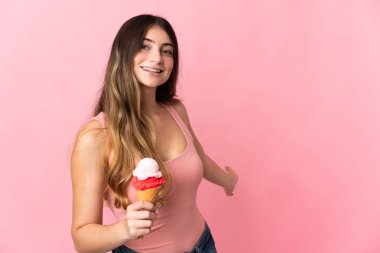 Kornet dondurması olan beyaz bir kadın pembe arka planda izole edilmiş. Gelmesi için ellerini yana uzatıyor.
