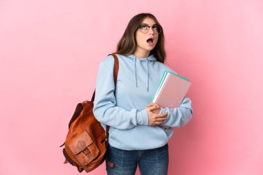 Pembe arka planda izole edilmiş genç bir bayan yukarı bakıyor ve şaşırmış bir ifadeyle