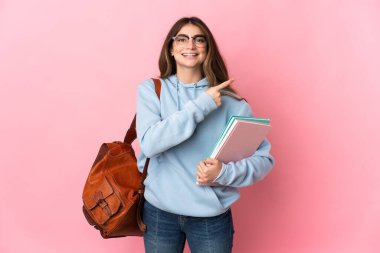 Pembe arka planda izole edilmiş genç bayan bir ürünü sunmak için kenarı işaret ediyor.