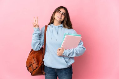 Pembe arka planda izole genç bayan gülümseyerek ve zafer işareti göstererek