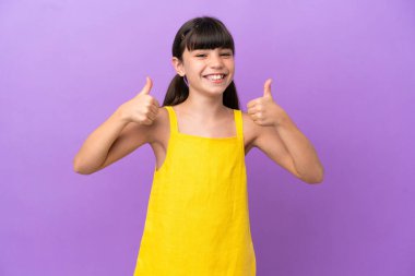 Küçük beyaz bir çocuk mor arka planda izole edilmiş bir şekilde baş parmak hareketi yapıyor.