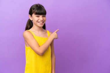 Mor arka planda izole edilmiş küçük beyaz çocuk bir ürünü sunmak için kenarı işaret ediyor.