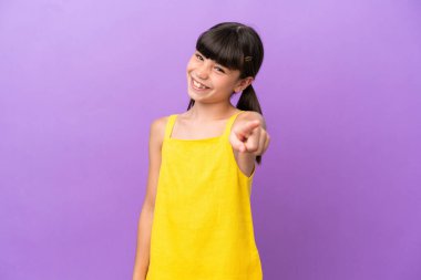 Mor arka planda izole edilmiş küçük beyaz çocuk mutlu bir ifadeyle öne işaret ediyor.