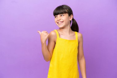 Mor arka planda izole edilmiş küçük beyaz çocuk bir ürünü sunmak için kenarı işaret ediyor.